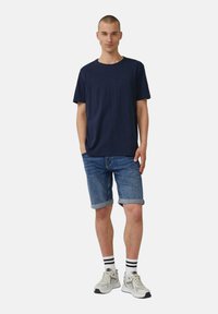 Navy blue cotton t-paita, farkkuhameet käännetyillä helmillä, harmaat lenkkarit ja raidalliset sukat. Yksinkertainen, rento asu ilman näkyviä logoja.