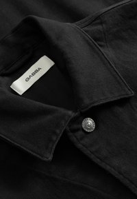 Black denim jacket collar with metal button and white fabric label showing brand name "GABBA."
