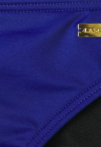 Parte de baixo de biquíni azul com tecido suave e texturizado. Apresenta um detalhe em metal dourado com o logótipo e forro preto. A costura é limpa e consistente.