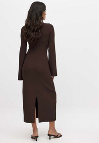 Ribattu pitkähihaine mekko ruskeana, jossa on takareikä ja tiukka siluetti, yhdistetty mustiin korkokenkiin. Huomattavissa on teksturoitu kangas.