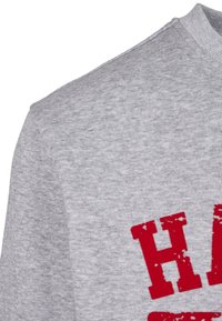 Tissu gris en gros plan avec des lettres rouges en bloc partiellement visibles et usées sur un sweat-shirt ou un pull.