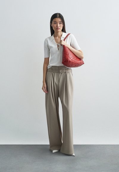 Piros szőtt kézi táska, rövid ujjas fehér, bordás póló csipkés részletekkel, bézs, magas derékú, bő szárú nadrág és hegyes orrú fehér lábbeli.