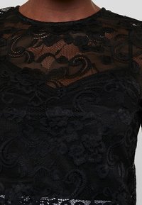 Schwarzes Spitzentop mit filigranen Blumenmustern und transparenter Textur. Abgerundeter Ausschnitt und kurze Ärmel. Geschichtetes, elegantes Design.