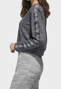 Sudadera gris de manga larga con tejido texturizado, que presenta rayas laterales negras con acentos de logo blanco. Joggers grises con estampado complementan el atuendo.