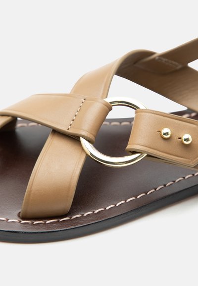 Ταμπά δερμάτινο σανδάλι με σταυρωτούς ιμάντες, χρυσό κυκλικό μεταλλικό δαχτυλίδι και ραμμένη σκούρα καφέ σόλα.
