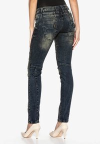 Schlanke Jeans aus Denim in dunkelblauer Waschung, mit verwaschenen Details, Gesäßtaschen und hohem Bund. Getragen mit beigen High Heels.