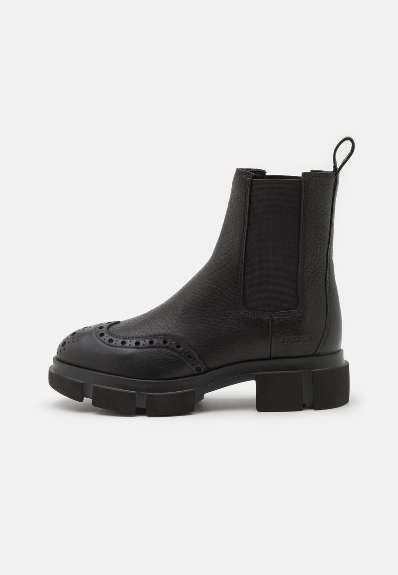 Botte Chelsea en cuir noir avec perforations brogue, panneaux latéraux élastiques, languette de tirage et semelle épaisse à crampons, vue de profil.