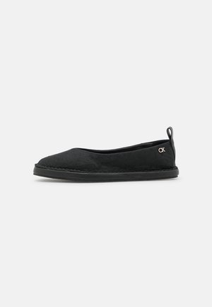 Sort slip-on flad sko med tekstureret stof, rundet tå, gummisål, trækflap ved hælen og lille metallisk "CK"-logo på siden.
