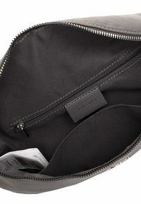 Atvērta pelēka soma ar melnu iekšpusi, kurā redzama kabata ar rāvējslēdzēju un iekšējā kabata ar salocītiem papīra priekšmetiem.