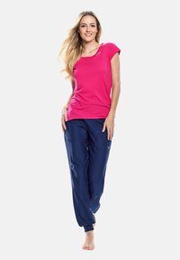 Rosa, kortärmad t-shirt med rund halsringning i kombination med marinblå, smalare sweatpants med mudd och synliga fickor, som visas av en modell.