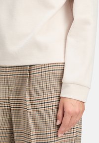 Jasno beżowy top z prążkowanej tkaniny z długimi rękawami, połączony z szerokimi spodniami w kratę w odcieniach beżu i czerni. Miękka tekstura, luźny krój.