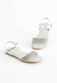 Zilveren platte sandalen met een metalen band en een gestructeerde stoffen strip. Vierkante neusontwerp en een enkelsluiting voor aanpassing.