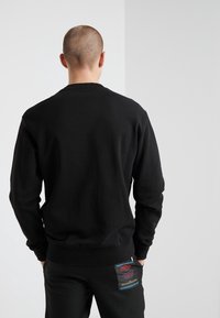 Sudadera de algodón negra con mangas largas y cuello redondo. Presenta puños y dobladillo acanalados. La vista trasera muestra una textura suave.