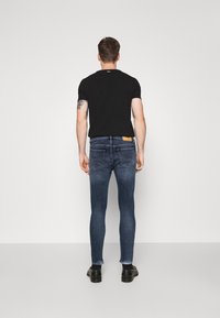 Slim-fit blå denimjeans med en ljus tvätt, stylande en svart t-shirt med kort ärm och svarta skor. Har en bakficketikett.
