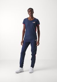 Conjunto deportivo en color navy que incluye una camiseta de manga corta con acentos rojos y pantalones a juego. El material es ligero y transpirable.