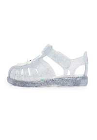 Clear, glittery sandals with a closed toe, open sides, adjustable strap, and a textured sole featuring a sparkly, translucent finish.