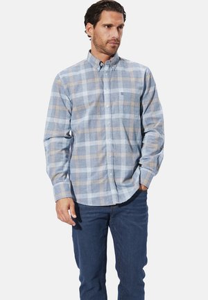 Langärmliges kariertes Hemd in Hellblau und Beige, mit einem Button-Down-Kragen und einem kleinen Logo-Patch, kombiniert mit dunkelblauen Jeans.