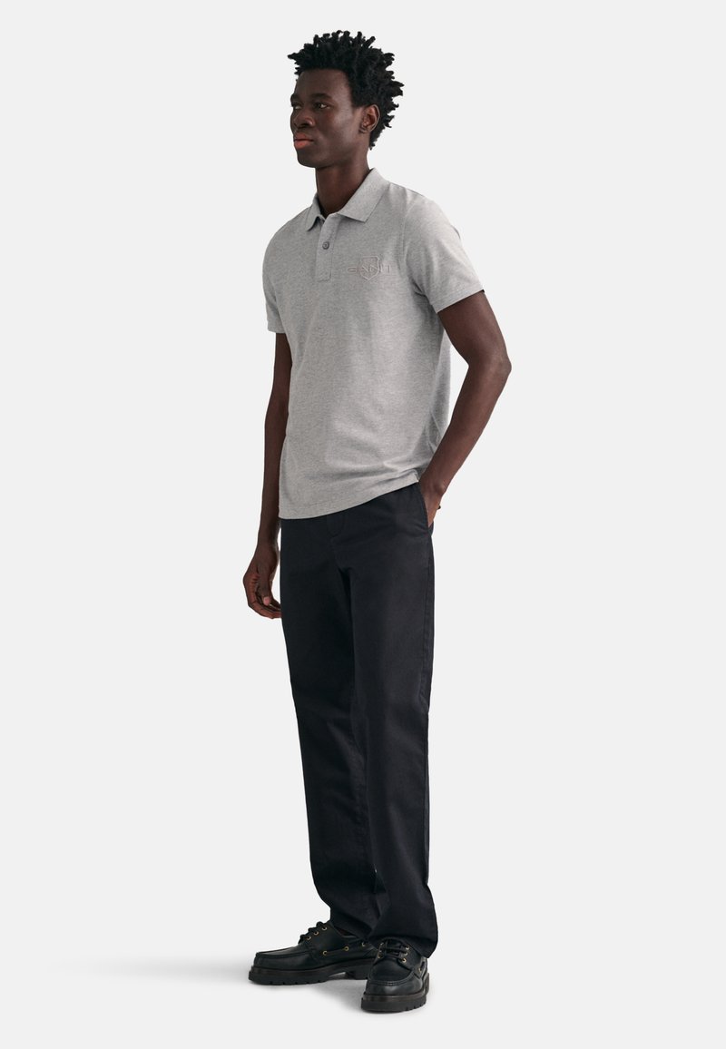 Szara koszulka polo z krótkim rękawem z subtelnym logo, w połączeniu z czarnymi spodniami i czarnymi butami, charakteryzująca się klasycznym krojem i prostym designem.