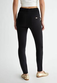 Melnas stiepjošās leggingas ar augstu jostasvietu, diviem aizmugurējiem kabatām un nelielu metāliski zeltītu logotipu labajā kabatā.