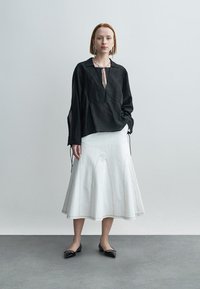 Blouse en lin noir avec ouverture à l'avant et détails à cordon, associée à une jupe blanche évasée avec coutures apparentes et texture lisse.