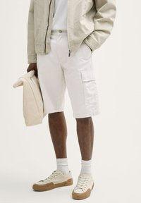 Vita cargo shorts med sidofickor, kombinerat med en lätt jacka och beiga sneakers. Outfiten har en avslappnad, ledig passform.