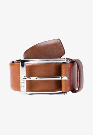 Brunt læderbælte rullet sammen med skinnende sølvfarvet rektangulært spænde og røde syninger nær løkken mod hvid baggrund.