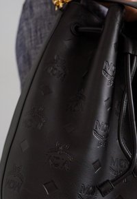 Borsa a secchiello in pelle nera con motivi del logo impressi, texture liscia, chiusura a coulisse e piccoli dettagli in oro.