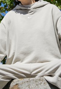 Light grey hoodie made of soft fabric, featuring a white Nike logo. The design includes a kangaroo pocket and a relaxed fit.