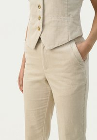Beige corduroy vest en broek met een subtiele ribbel textuur. Knopen in een lichtbruine tint, met zijkanten zakken op de broek.
