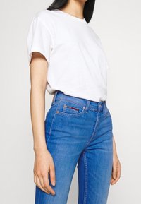 Camiseta de algodón blanca con mangas cortas, combinada con jeans azules de cintura alta. Los jeans tienen un diseño clásico y costuras sutiles.