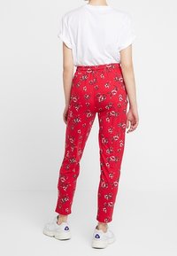 Röda blommiga elastiska midjebyxor i mjukt tyg med smal passform, kombinerat med en kontrasterande vit t-shirt och vita sneakers.