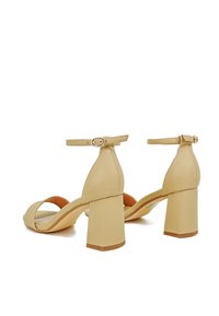 Sandali beige con tacco a blocco e cinturini alla caviglia, realizzati in pelle liscia. Presentano un punta aperta e un design minimalista per un aspetto pulito.