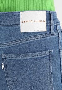 Vaqueros de denim con un lavado azul claro, que presentan una etiqueta de cuero blanca que dice "LEVI'S LINE 8" y un bolsillo trasero con costura curvada.