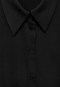 Blouse noire à la texture lisse, avec un col classique et cinq boutons noirs sur le devant. Design minimaliste, sans motifs.