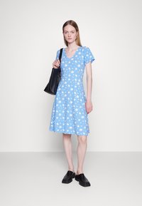Vestido floral azul com mangas curtas, decote em V e saia rodada. Combinado com uma mala de tote preta e sapatos slip-on pretos.