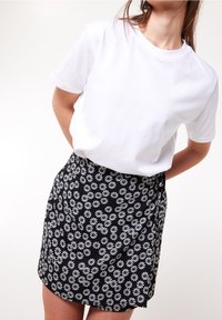 Bílá bavlněná trička v kombinaci s černou sukní s bílým květinovým vzorem sedmikrásky, obojí jednoduché a ležérní v designu.