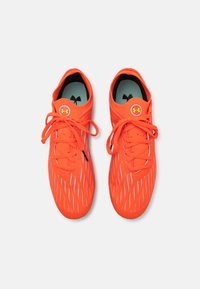Scarpe sportive di un vivace arancione con un design elegante, dotate di una tomaia testurizzata, accenti neri a contrasto e un logo circolare sulla linguetta.