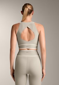 A világosszürke sportmelltartó és a hozzá illő leggings kivágott hátrésszel, sima textúrával és kontrasztos díszítéssel rendelkezik. A márkajelzés a derékpánton látható.