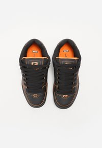Black sneakers with orange accents, textured synthetic upper, lace-up design, padded collar, and logo detail on the tongue and side.