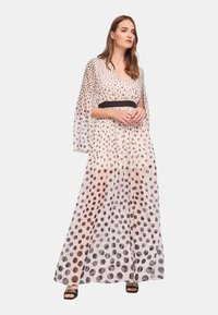 Lungo vestito trasparente con motivo a pois in diverse sfumature di marrone su uno sfondo chiaro. Presenta un profondo scollo a V e una vita cintrata.