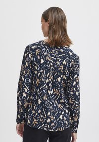 Camicia a maniche lunghe realizzata in tessuto blu navy con un motivo astratto colorato in beige e azzurro chiaro. Include un giogo posteriore e dettagli arricciati.