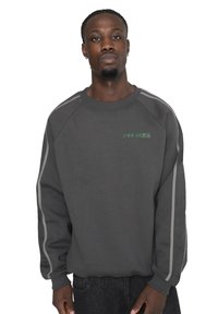 Sudadera gris de algodón, con mangas raglán y texto verde en el pecho. Incluye franjas laterales blancas para contraste.