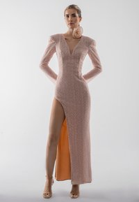 Gara, pieguļoša kleita gaiši rozā audumā ar reljefu rakstu, dziļu V veida izgriezumu, garām piedurknēm un augstu sānu šķēlumu, kas atklāj oranžu oderi.