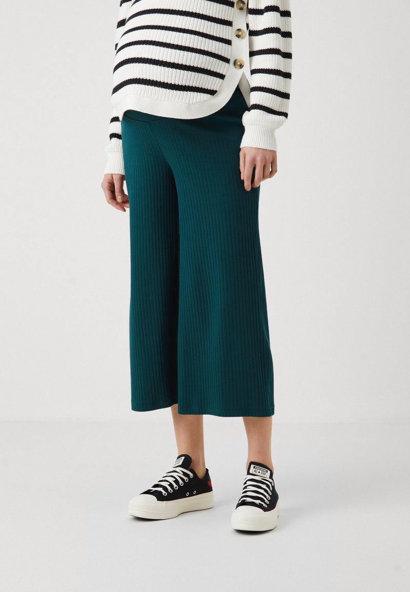 Teal ribbede culotter parret med en sort-hvid stribet strikcardigan og sorte sneakers med hvide såler. Glat tekstur, afslappet stil.