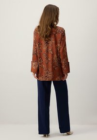 Bluza maro cu model floral, cu mâneci lungi și manșete largi, asortată cu pantaloni bleumarin. Textură fină și croială lejeră.