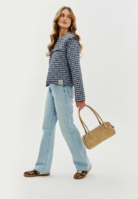 Koszula w kratę z długim rękawem w kolorze granatowym i białym, jasnoniebieskie dżinsy, beżowa torebka i trampki w panterkę. Nowoczesny, casualowy zestaw.