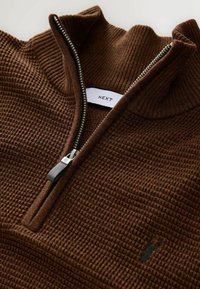 Brauner strukturierter Reißverschluss-Pullover mit geripptem Kragen und silbernem Reißverschluss. Mit dezentem, gesticktem Logo auf der Vorderseite. Markentag im Kragen sichtbar.