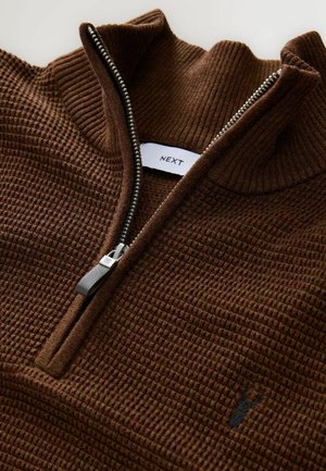 Brun, struktureret zip-sweater med ribkant på kraven og sølvfarvet lynlås. Har et subtilt broderet logo på forsiden. Mærketikette synlig i kraven.