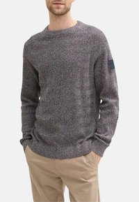 Pull en tricot avec un motif en chevron multicolore, col rond, manches longues, poignets côtelés et un petit logo brodé sur la manche gauche.