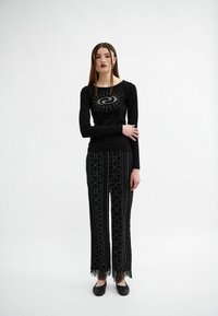Schwarzes Langarmshirt mit kreisförmigem Strassdesign, kombiniert mit schwarzen Hosen mit Spitzenbesatz und bestickten Blumenmustern.